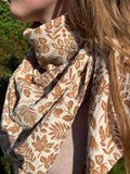 Chèche triangle en gaze de coton avec un motif végétal imprimé dans des tons de marron et beige, porté autour du cou par une jeune femme.