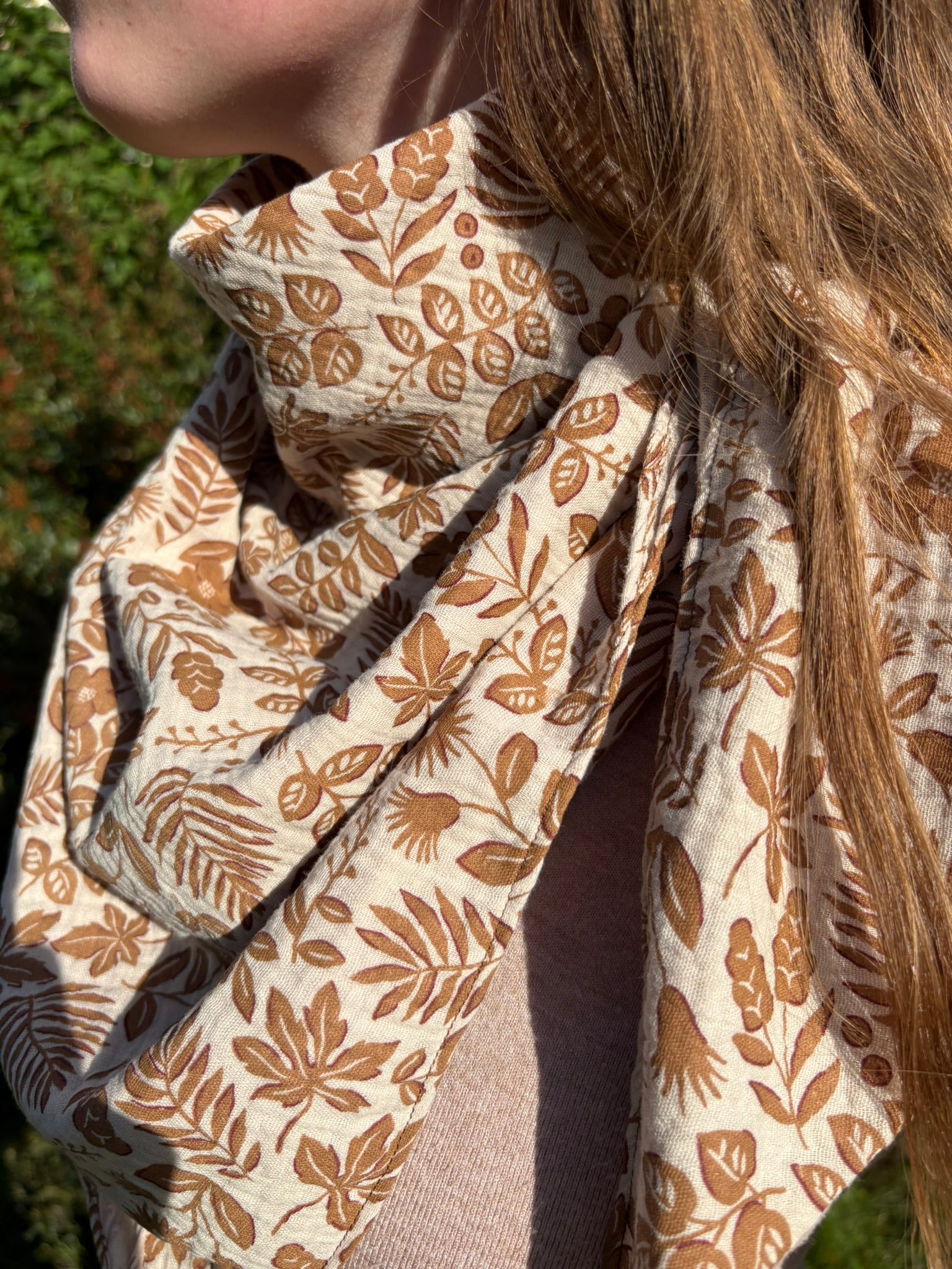 Chèche triangle en gaze de coton avec un motif végétal imprimé dans des tons de marron et beige, porté autour du cou par une jeune femme.