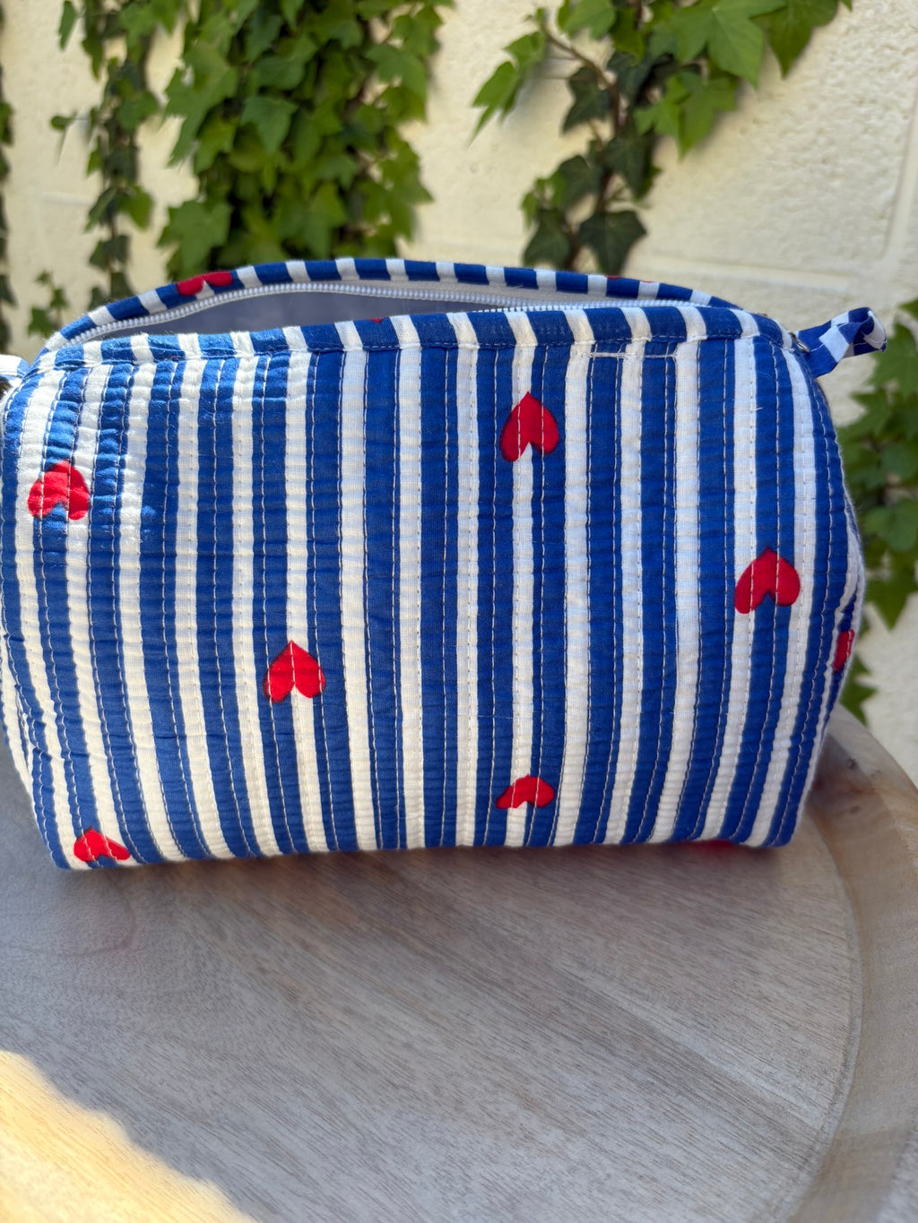 Une trousse de toilette en coton matelassé bleu et blanc à rayures, imprimée de petits cœurs rouges en blockprint artisanal