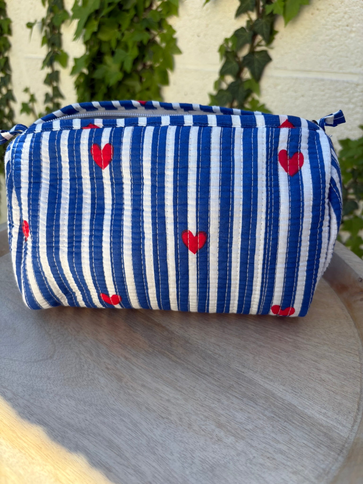 Une trousse de toilette en coton matelassé bleu et blanc à rayures, imprimée de petits cœurs rouges en blockprint artisanal