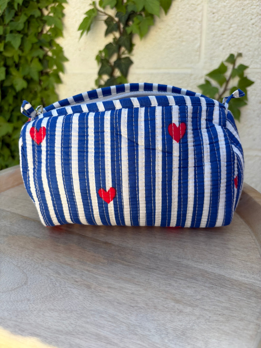 Une trousse de toilette en coton matelassé bleu et blanc à rayures, imprimée de petits cœurs rouges en blockprint artisanal