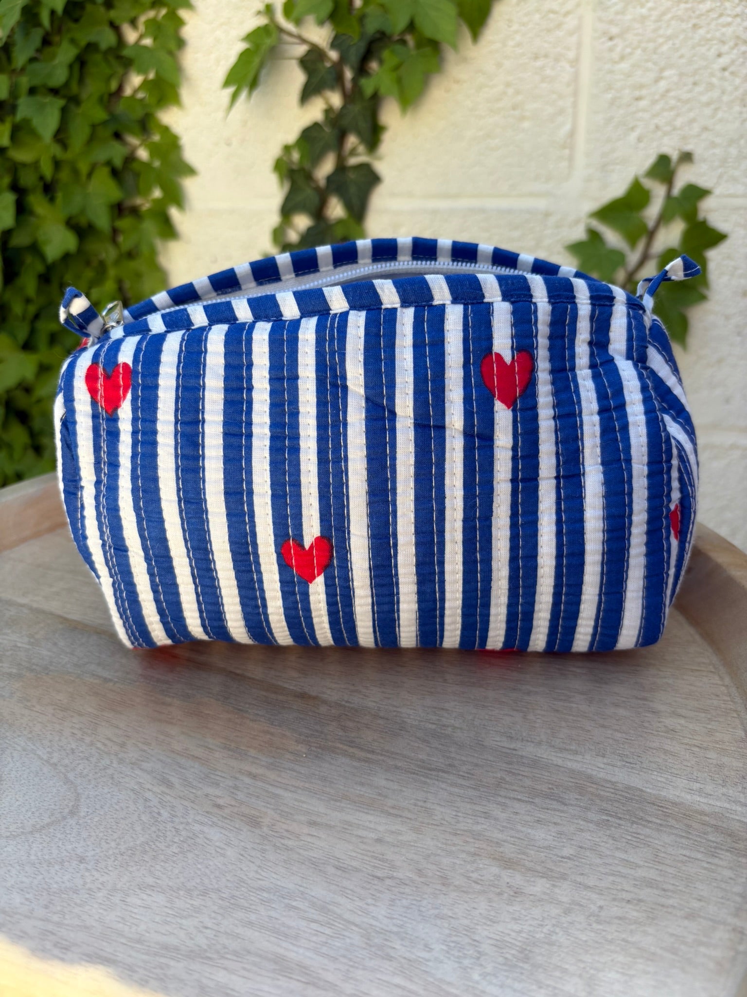 Une trousse de toilette en coton matelassé bleu et blanc à rayures, imprimée de petits cœurs rouges en blockprint artisanal
