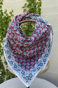 Un grand foulard en coton léger est drapé artistiquement sur un support en bois. Le motif central du foulard présente des feuillages stylisés bleu canard et gris répétés sur un fond lie de vin (vieux rose foncé). Le foulard est encadré par une large bordure blanche ornée de fleurs indiennes complexes et de motifs de médaillons, imprimés dans les mêmes tons de bleu et de lie de vin. La technique est de l'impression artisanale blockprint.  