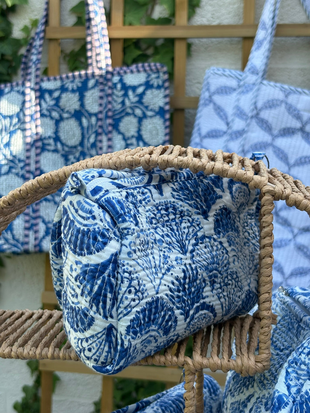 Trousses de toilette matelassées en coton blanc avec motifs coquillage bleu indigo imprimés au blockprint artisanal, présentées sur une étagère ronde en rotin tressé.