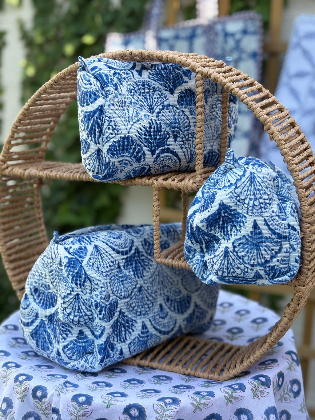 Trousses de toilette matelassées en coton blanc avec motifs coquillage bleu indigo imprimés au blockprint artisanal, présentées sur une étagère ronde en rotin tressé.
