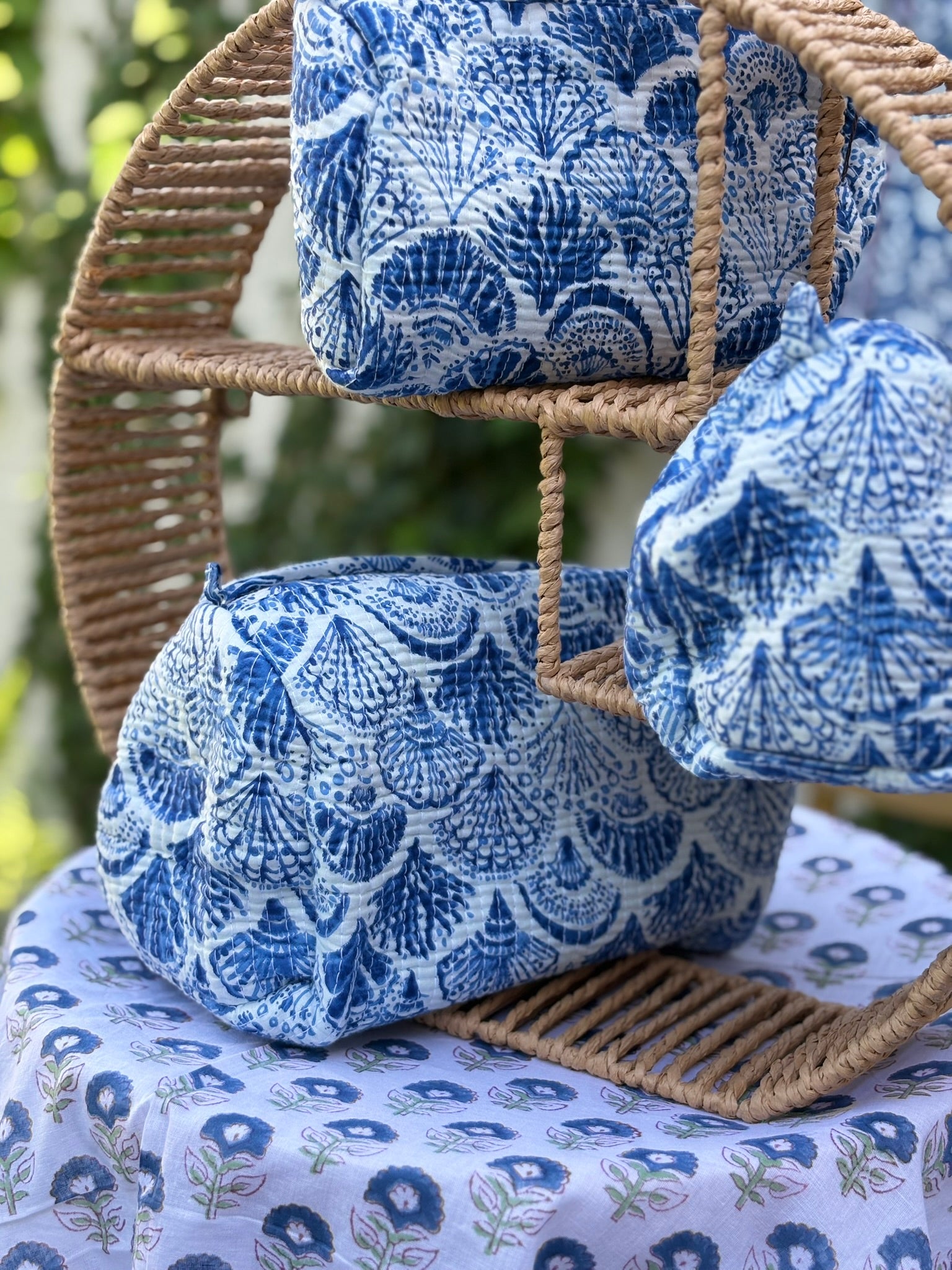 Trousses de toilette matelassées en coton blanc avec motifs coquillage bleu indigo imprimés au blockprint artisanal, présentées sur une étagère ronde en rotin tressé.