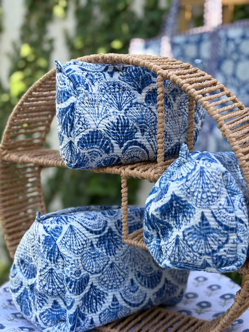 Trousses de toilette matelassées en coton blanc avec motifs coquillage bleu indigo imprimés au blockprint artisanal, présentées sur une étagère ronde en rotin tressé.