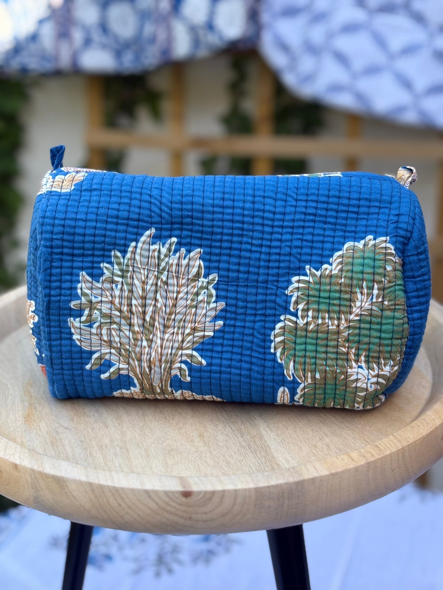 Une trousse de toilette en coton matelassé bleu avec motifs d'arbres et feuillages végétaux ocre et vert, imprimée en blockprint artisanal sur une table ronde