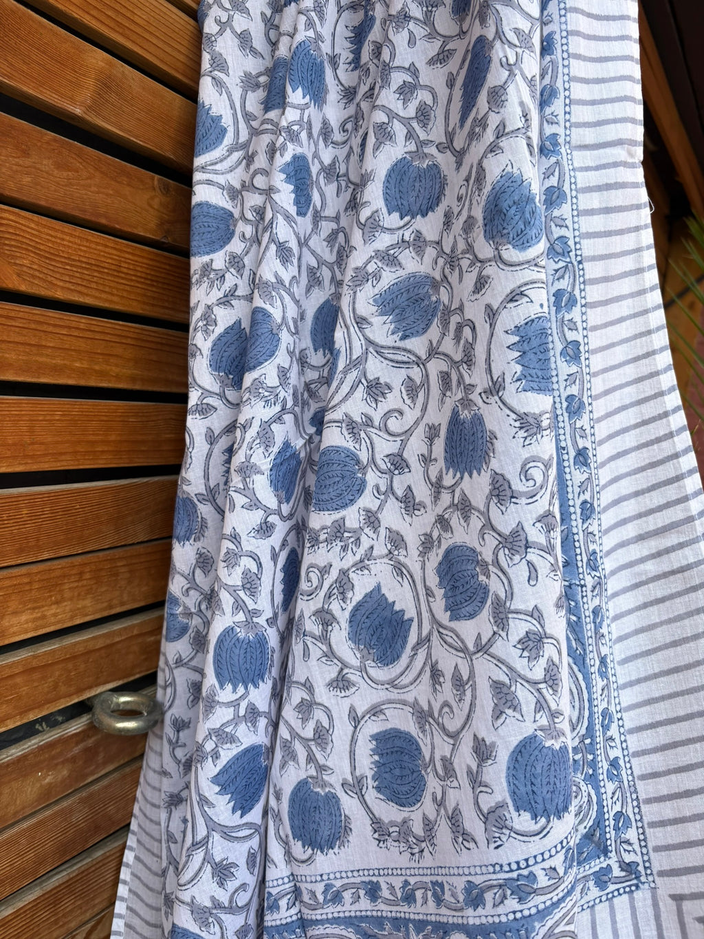 Paréo en coton léger avec impression artisanale indienne de type block print. Il présente un motif floral et végétal détaillé aux teintes bleu ardoise et gris sur un fond blanc, structuré par de larges bordures ornées et des finitions à fines rayures. 