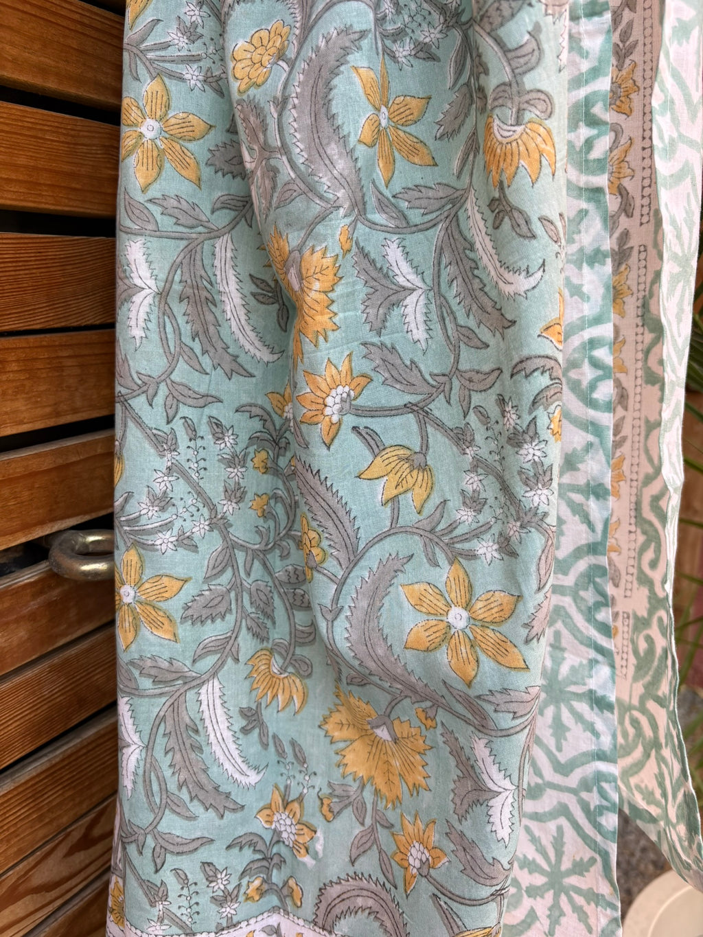 Paréo en coton léger avec impression artisanale indienne de type block print. Il présente un motif floral et végétal aux teintes jaune et gris-vert sur un fond vert d'eau clair, associé à des bandes de motifs géométriques inspirés des carreaux traditionnels. 