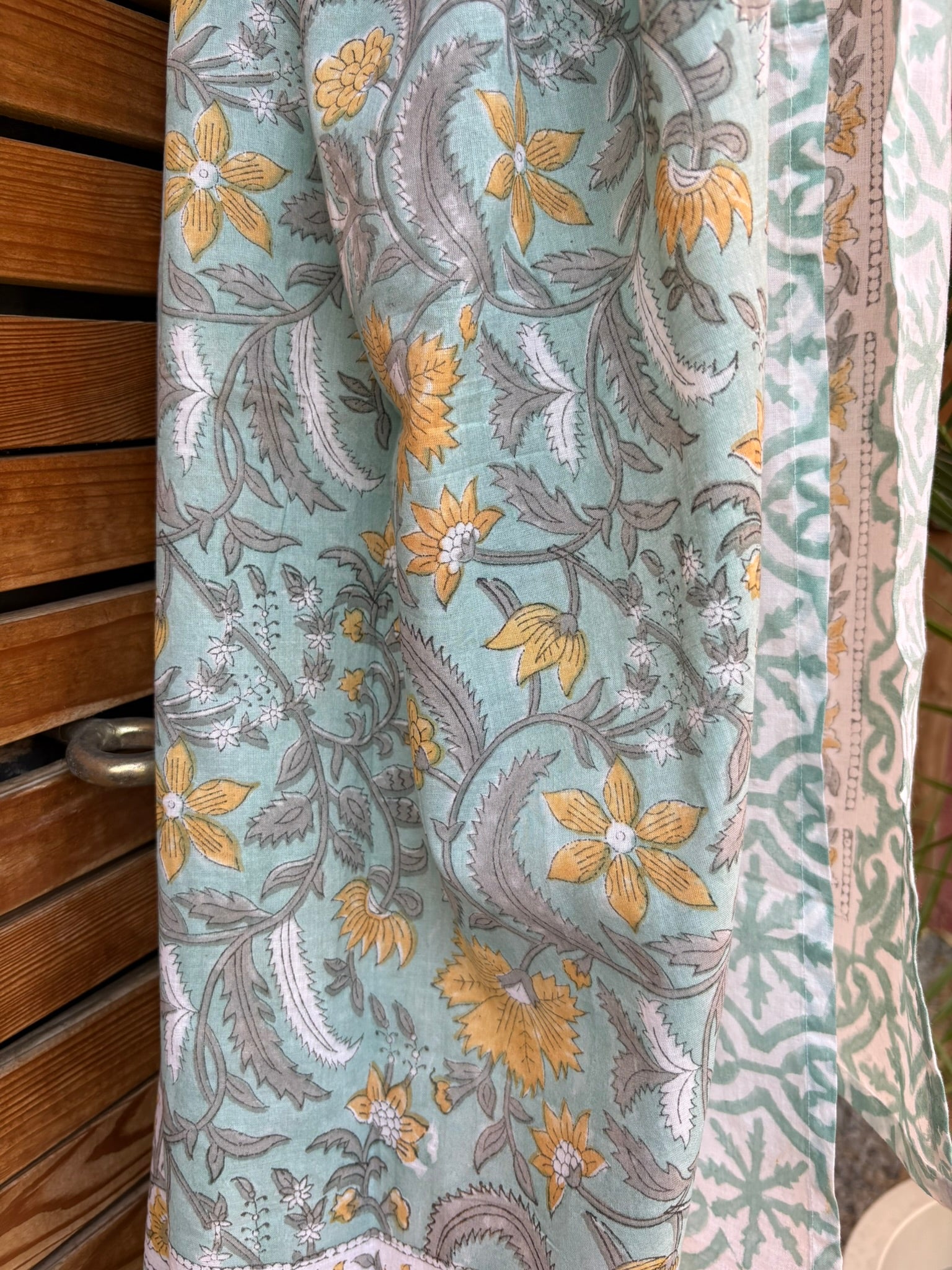 Paréo en coton léger avec impression artisanale indienne de type block print. Il présente un motif floral et végétal aux teintes jaune et gris-vert sur un fond vert d'eau clair, associé à des bandes de motifs géométriques inspirés des carreaux traditionnels. 