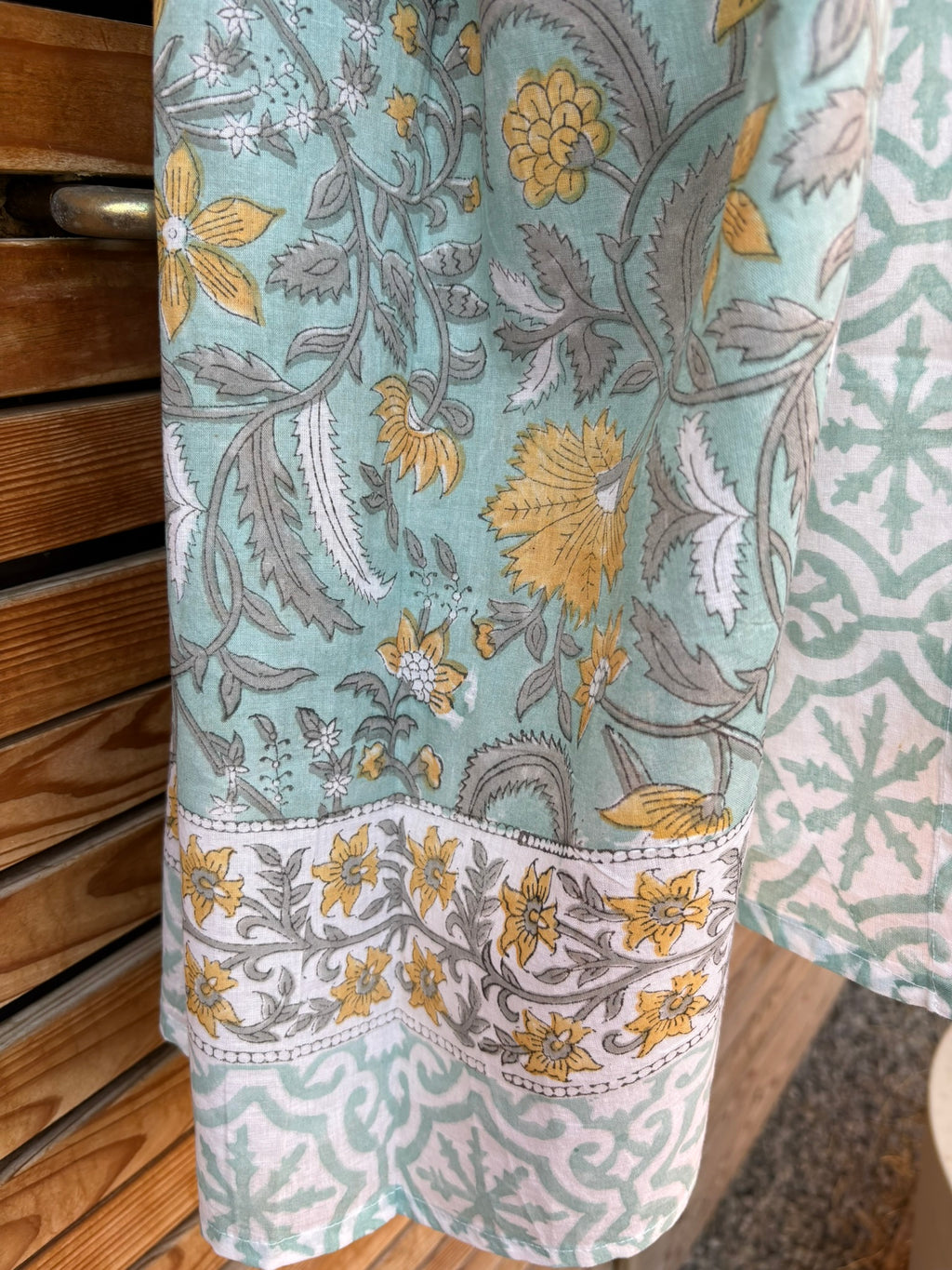 Paréo en coton léger avec impression artisanale indienne de type block print. Il présente un motif floral et végétal aux teintes jaune et gris-vert sur un fond vert d'eau clair, associé à des bandes de motifs géométriques inspirés des carreaux traditionnels. 