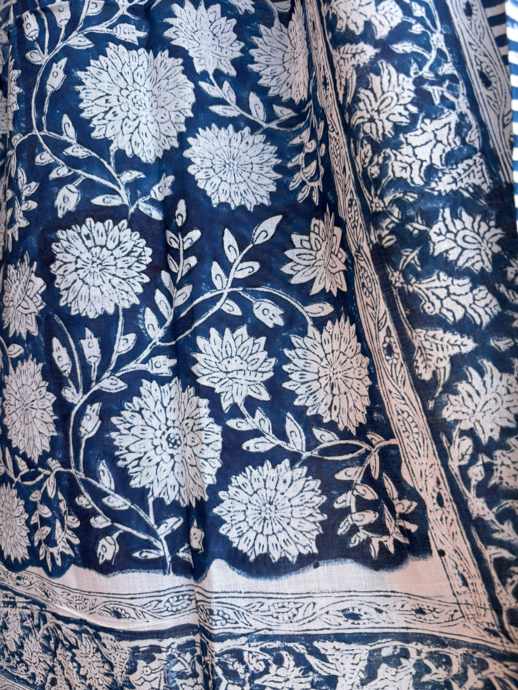 Paréo en coton léger avec impression artisanale indienne de type block print, présentant un motif floral complexe et dense de couleur blanc cassé sur un fond bleu indigo profond. Le tissu est bordé de bandes à rayures fines assorties. 